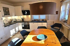 Una cuina moderna amb armaris blancs, una taula de dinar de fusta i una llum penjant gran.
