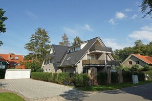 Ein zweigeschossiges Wohnhaus mit Satteldach, einer Veranda und einem eingezäunten Garten.