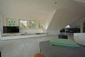 Ein modernes Wohnzimmer mit Flachbildfernseher, einer Couch, einem Couchtisch und einer Essecke mit Tisch und Stühlen.