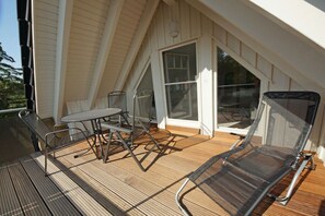 Eine überdachte Terrasse mit Tisch und Stühlen, eine Glastür zum Innenbereich und Blick ins Freie.