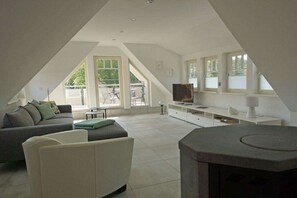 Ein modernes Wohnzimmer im Loft-Stil mit hohen Decken, Kamin, einer Couch, einem Fernseher und großen Fenstern.