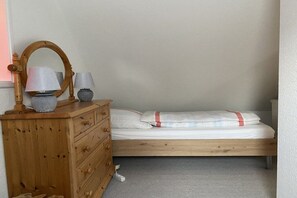 A bedroom with a wooden dresser, a bed with a white mattress and red-striped pillow, and two lamps. - Holiday home with 2 bedrooms (Stedesand)