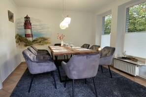 A dining area with a table, chairs, and a painting of a lighthouse. - Holiday home with 2 bedrooms (Stedesand)