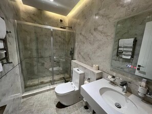 A modern bathroom with a glass-enclosed shower, a white toilet, a sink, and a mirror. - Pana Hotel (Nukus)