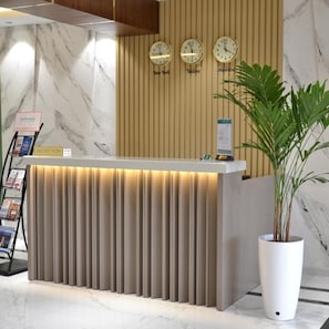 A reception desk with a marble wall, three clocks, and a reception sign. - Pana Hotel (Nukus)