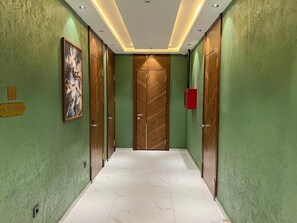 A hallway with green walls, wooden doors, and a marble floor. - Pana Hotel (Nukus)