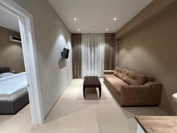 A hotel room with a bed, a sofa, a coffee table, and a TV mounted on the wall. - Pana Hotel (Nukus)