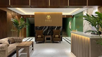 A hotel reception area with a reception desk, two armchairs, a sofa, and a coffee table.