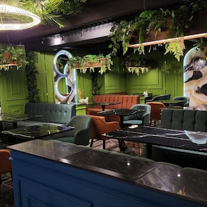 A restaurant interior with green walls, a circular seating area, and hanging plants. - Pana Hotel (Nukus)