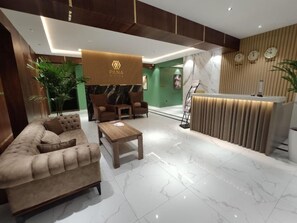 Un hall d’hôtel moderne avec un comptoir d’accueil, un espace salon et un mur d’accent vert.
