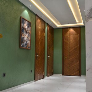 A hallway with green walls, wooden doors, and a marble floor. - Pana Hotel (Nukus)
