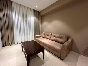 Een kamer met een bank en een tafel, een raam met gordijnen en een effen muur.