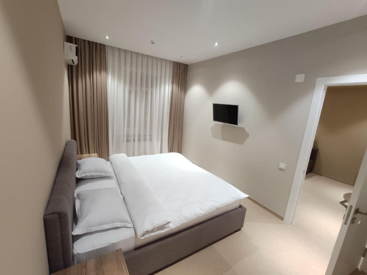 A modern bedroom with a bed, curtains, a mounted TV, and a door leading to another room.