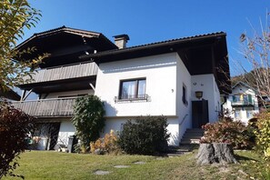 Ein zweistöckiges Gebäude mit Balkon, Eingangstür und einem kleinen Garten mit einem Baumstumpf.