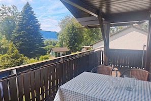 A balcony with a table and chairs, overlooking a mountainous landscape with trees and a small building. - Holiday apartment with 1 bedroom (Bodensdorf)