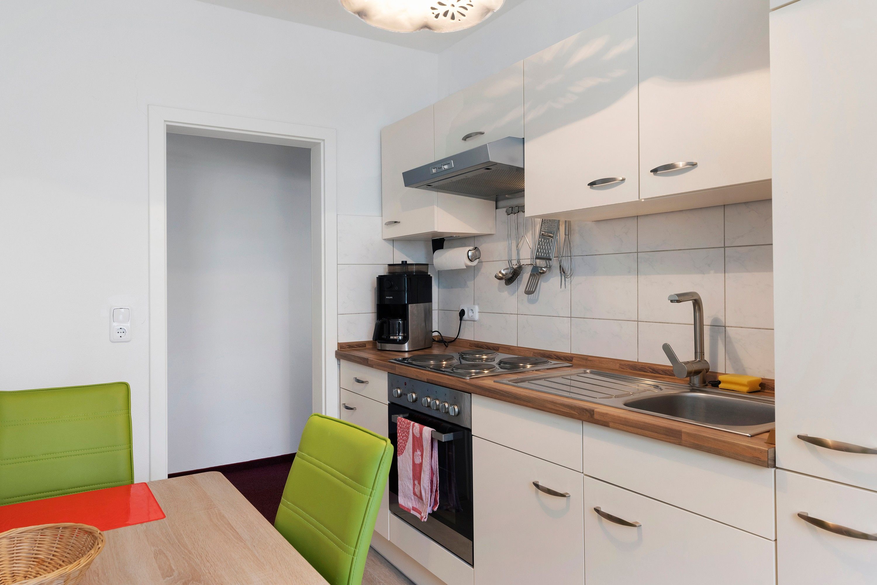 A compact kitchen with white cabinets, a built-in oven, a coffee maker, and a sink.