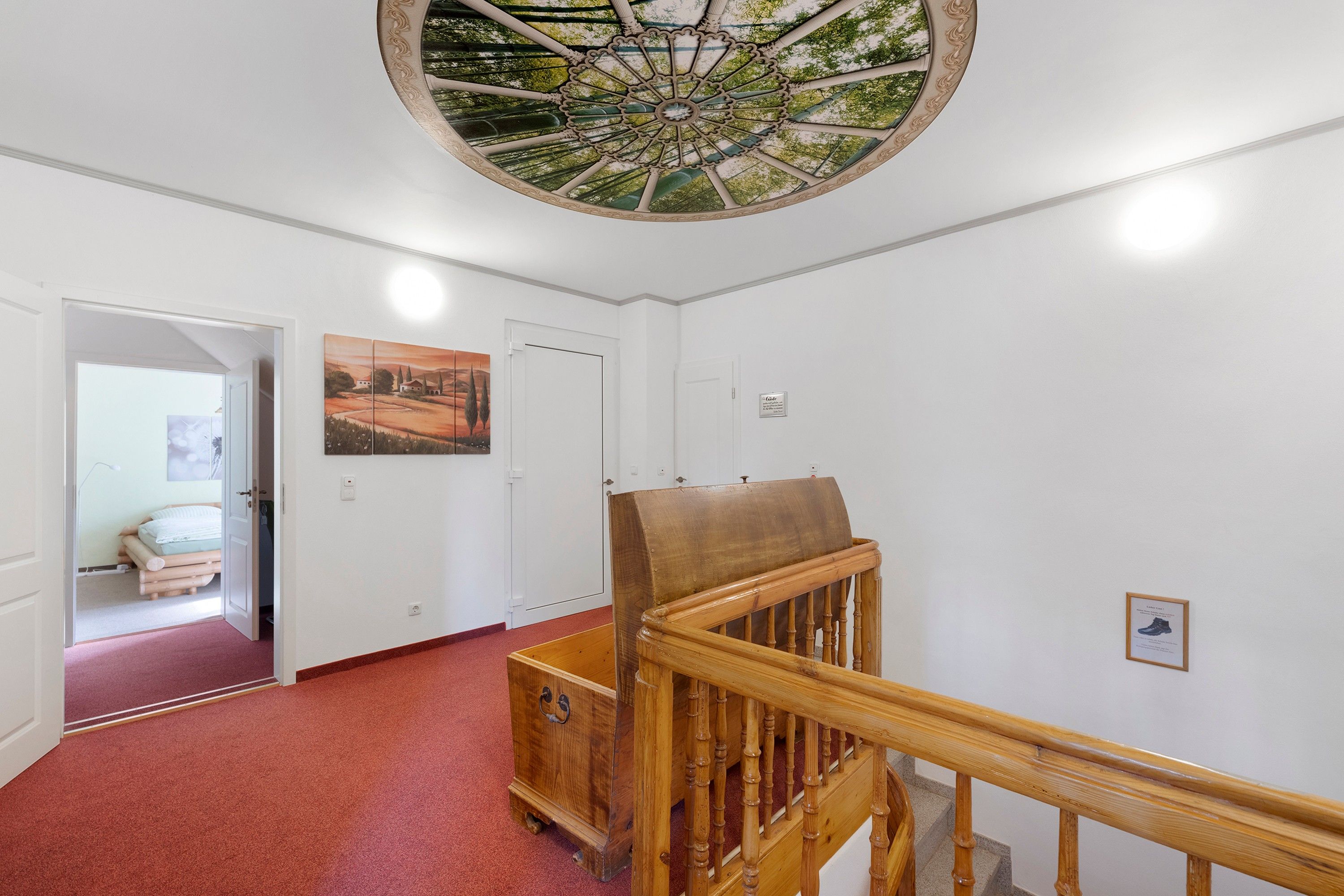 A hallway with a wooden staircase, a red carpet, a door, and a ceiling with a decorative design.