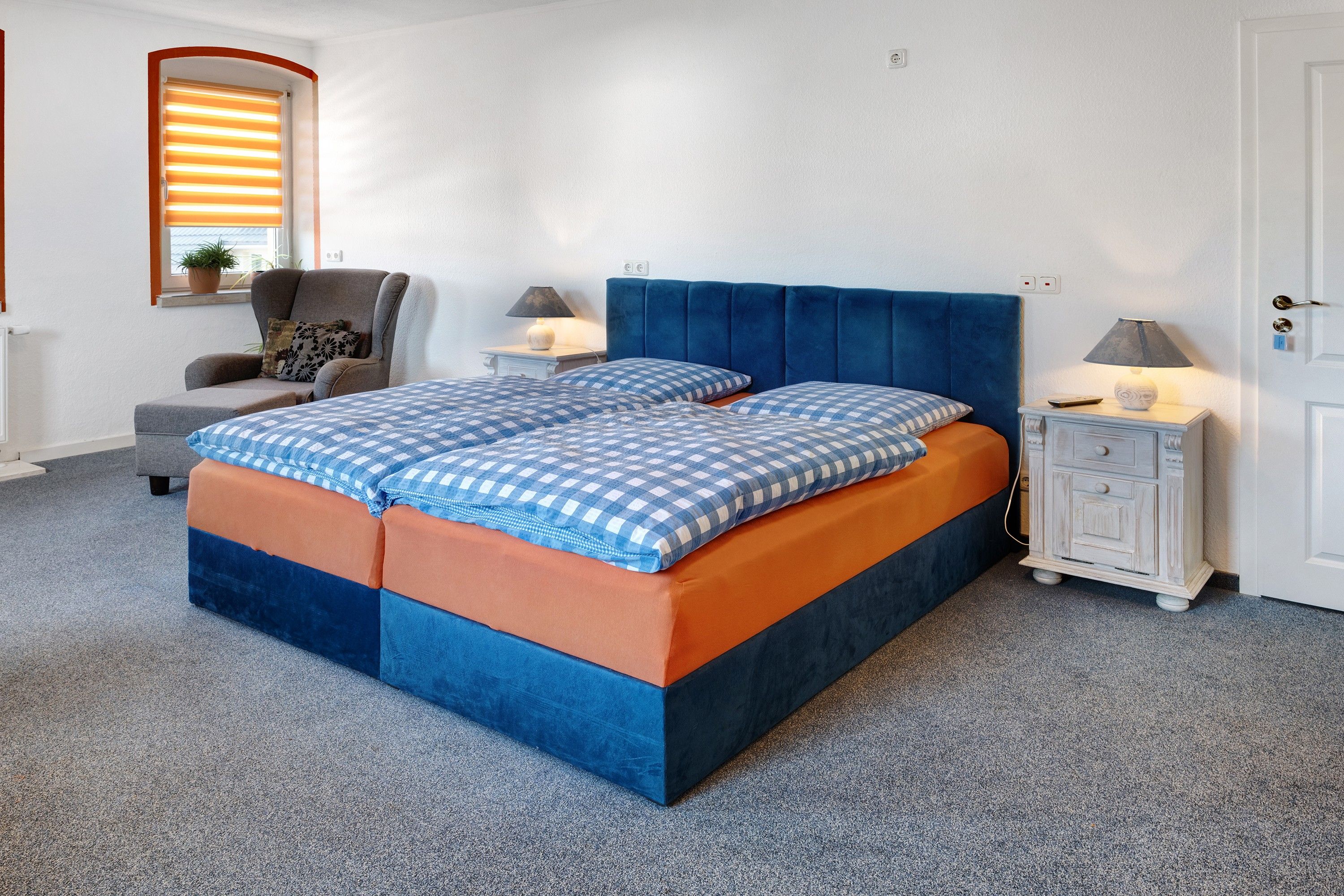 Ein Schlafzimmer mit einem Bett, zwei Nachttischen, einem Sessel und einer Lampe.