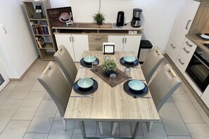 A modern kitchen with a dining table set for four, equipped with a coffee machine, a small plant, and a framed picture on the wall. - Holiday apartment in Norddeich with Wi-Fi (Norddeich)