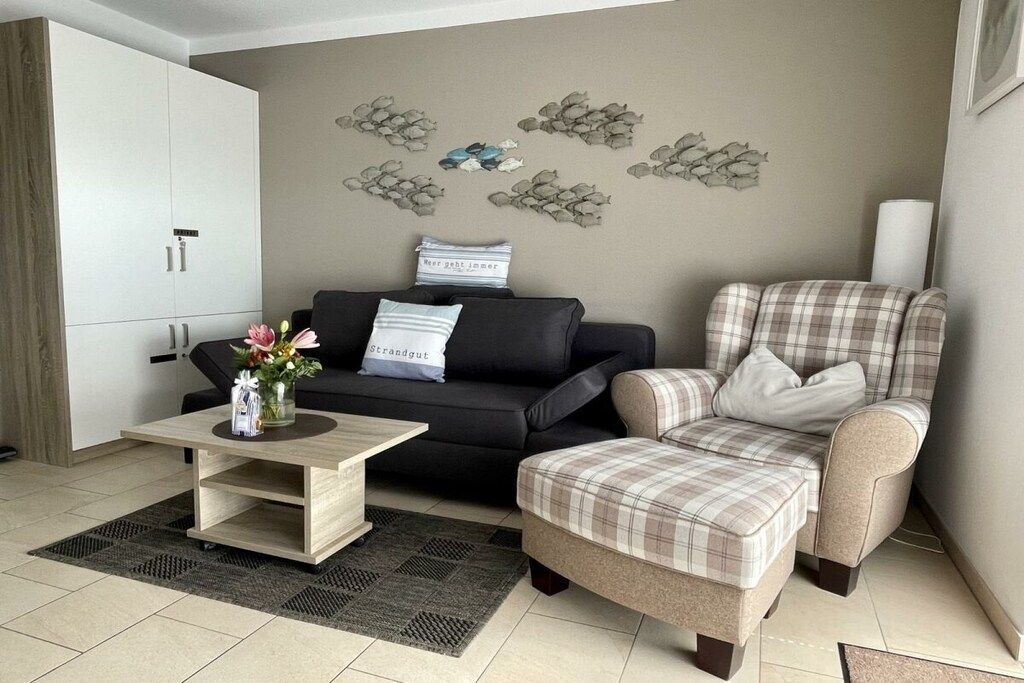 Un salon avec un canapé noir, un fauteuil à motifs, une table basse et un élément décoratif mural.
