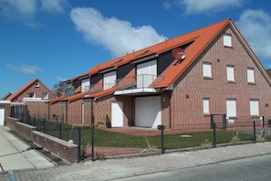 A two-story residential building with a red-tiled roof, a brick facade, and a fenced yard. - Holiday apartment in Norddeich with Wi-Fi (Norddeich)