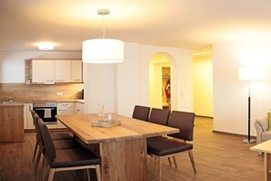 A modern kitchen with white cabinets, a wooden dining table with chairs, and a pendant light. - Holiday apartment in Mittelberg with Wi-Fi (Mittelberg)