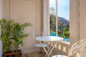 Un balcón con una mesa y sillas blancas, una planta en maceta y vistas a una colina.