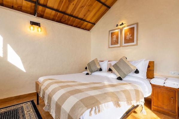 Un dormitorio con techo de madera, una cama con manta a rayas, dos lámparas fijadas a la pared y una mesita de noche con lámpara.