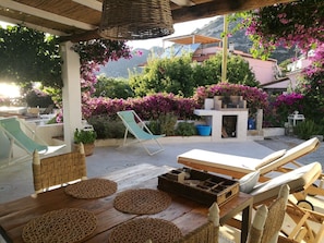 Eine Terrasss mit Liegestühlen, einem Tisch mit gewebten Unterlagen und einer Grillgegend.