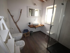 Ein Badezimmer mit einer weißen Toilette, einem Bidet, einem hölzernen Waschtisch mit Waschbecken und einer Duschkabine aus Glas.