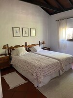 Un dormitorio con dos camas, una mesita de noche con lámpara y una ventana con cortinas.