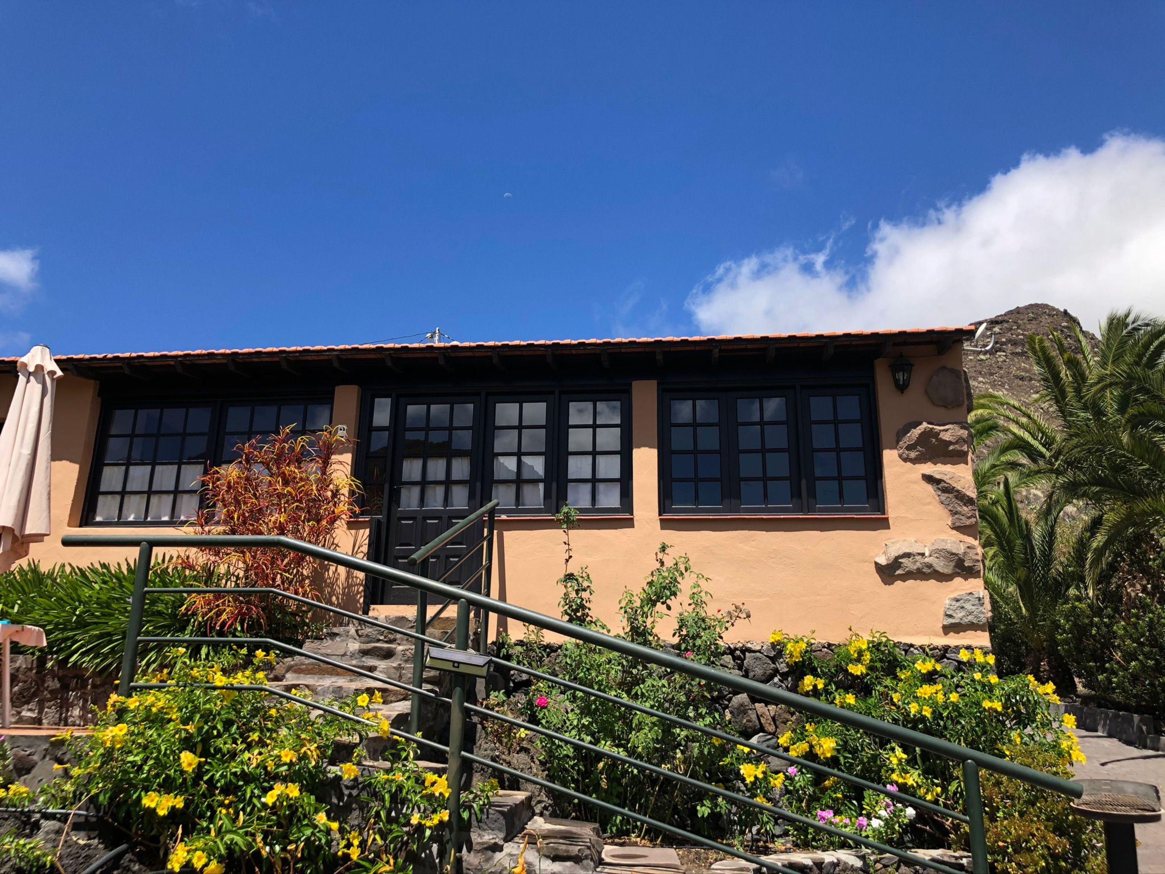 Un edificio con una escalera que lleva a una puerta, rodeado de flores amarillas y un cielo azul despejado.