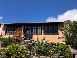 Un edificio con una escalera que lleva a una puerta, rodeado de flores amarillas y un cielo azul despejado.