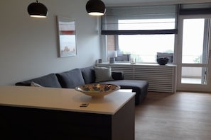 A modern living room with a sofa, a coffee table, and a large window with blinds. - Holiday apartment with 1 bedroom (Lübeck-Travemünde)