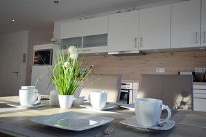 A modern kitchen with white cabinets, a wooden countertop, and a dining table set with white plates, cups, and a potted plant. - Holiday apartment with 1 bedroom (Norddeich)