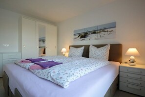 Een slaapkamer met een bed, twee nachtkastjes met lampen, een kledingkast en een aan de muur hangend kunstwerk.