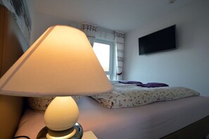 A bed with a floral-patterned pillow, a bedside lamp, and a television mounted on the wall. - Holiday apartment with 1 bedroom (Norddeich)