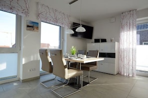 A modern kitchen with a dining area, including a table with chairs, a TV mounted on the wall, and a cabinet. - Holiday apartment with 1 bedroom (Norddeich)