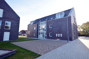 A modern building with a brick facade, large windows, and a gravel driveway. - Holiday apartment with 1 bedroom (Norddeich)