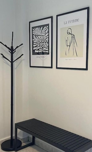 A room with a black floor lamp, a bench, and two framed artworks on the wall. - Marinos Rooms (Corinth)