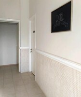 Un pasillo con piso de baldosas, una puerta blanca y un cartel enmarcado en la pared.