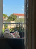 Ein Balkon mit gepolstertem Sitzplatz, einem Blumentopf und Blick auf ein Gebäude mit rotem Dach.