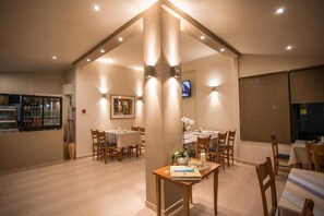 Un comedor con mesas y sillas, un refrigerador con bebidas, y un televisor en la pared.
