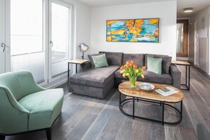 A modern living room with a grey sofa, a green armchair, and a coffee table with a vase of flowers. - Holiday apartment with 2 bedrooms (Norderney)