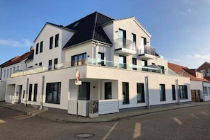 Ein zweigeschossiges Wohngebäude mit einem Balkon im oberen Stockwerk, einer Garagentür und blauem Himmel.