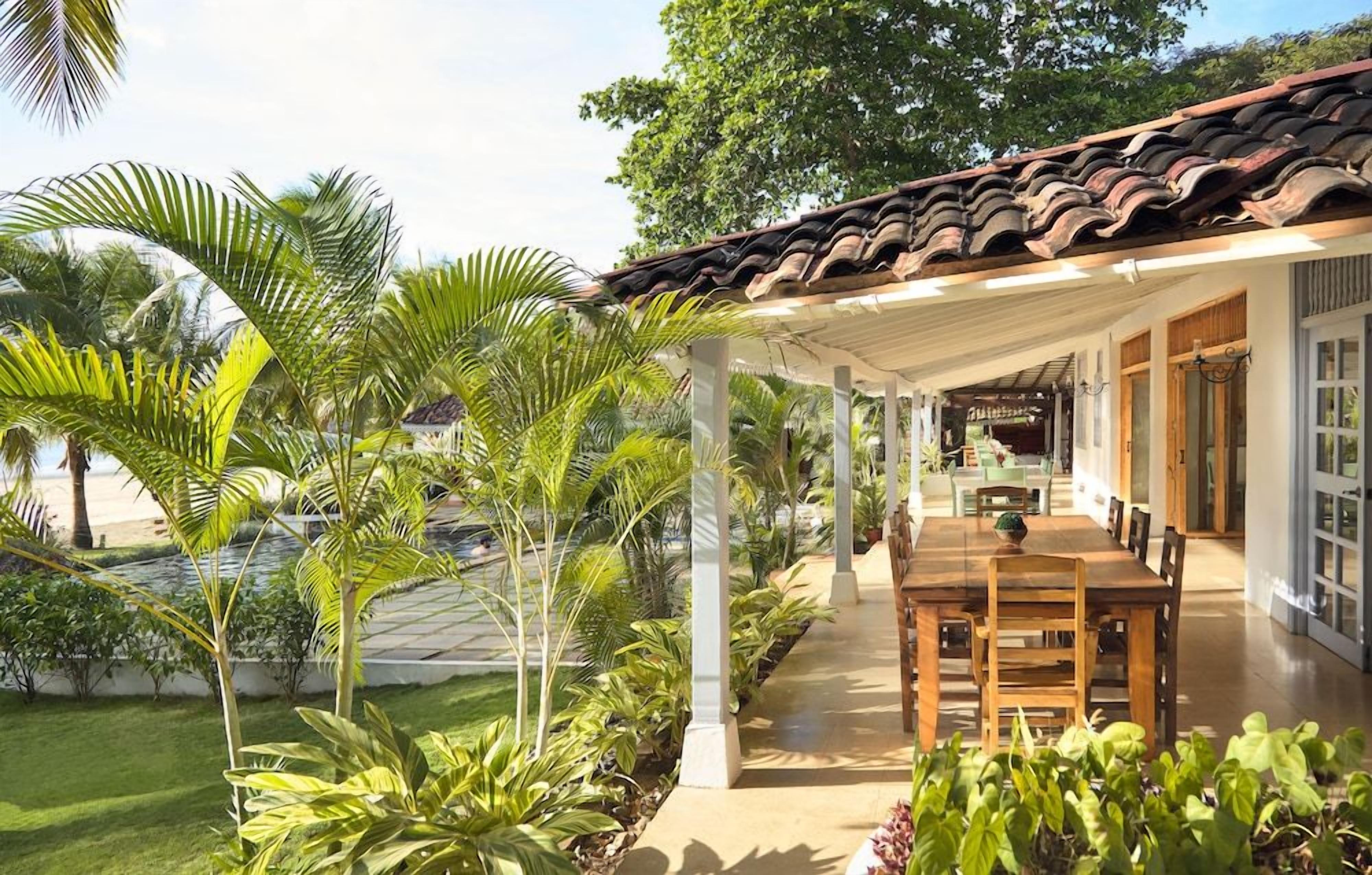 A covered outdoor dining area with a patio, surrounded by lush greenery and palm trees.
