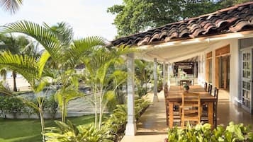 A covered outdoor dining area with a patio, surrounded by lush greenery and palm trees.