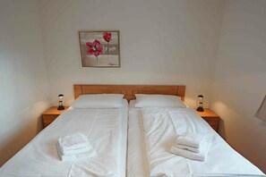 Ein Doppelbett mit weißer Bettwäsche, zwei Nachttische mit Lampen und ein Blumenbild an der Wand.