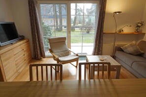 Ein Zimmer mit Fernseher auf einer Holzkommode, einem Sessel, einem Tisch, einer Couch und einer Lampe.