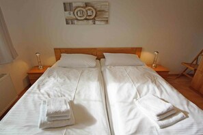 A double bed with white linens and towels, wooden headboard, bedside lamps, and a wall art piece. - Holiday apartment with 2 bedrooms (Prerow)